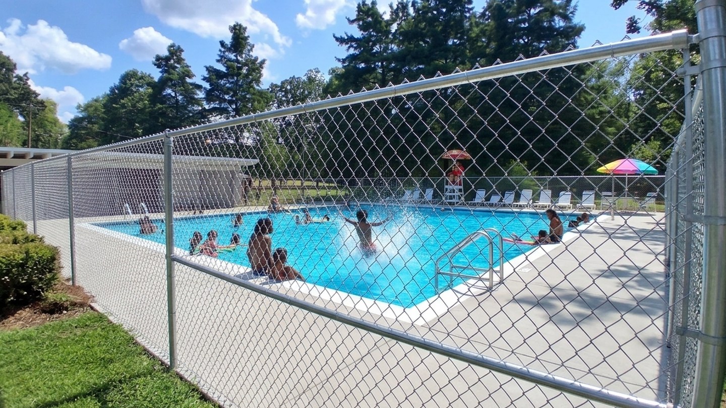 After: the rusted fence line of the closed Norwood pool, restored with clean fencing and a pool full of swimmers